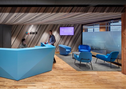 Press kit | 1513-01 - Press release | Slack Toronto Office - Dubbeldam Architecture + Design - Commercial Interior Design - Industrial felt lines the wall and ceiling of the reception area in a striated pattern by Felt Studio. The lowered ceiling offers a more intimate and welcoming area for guests, who are greeted by the custom faceted reception desk, the company logo, a television showcasing the company’s latest flattering “love tweets,” and seating by Bensen and Normann Copenhagen.  - Photo credit:  Shai Gil 