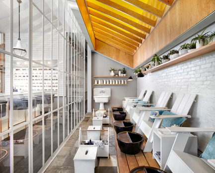 Press kit | 1048-08 - Press release | Reinventing the beauty salon experience with Her Majesty’s Pleasure - +tongtong - Commercial Interior Design - A long, raised wooden deck lined with Muskoka chairs defines the pedicure area. Above the deck, the coved ceiling is painted a fresh yellow and softly lit with a rafter-like structure assembled over top. The pedicure area, which was designed with an outdoor porch in mind, feels separate of the main area.&nbsp; <br> - Photo credit: Lisa Petrole