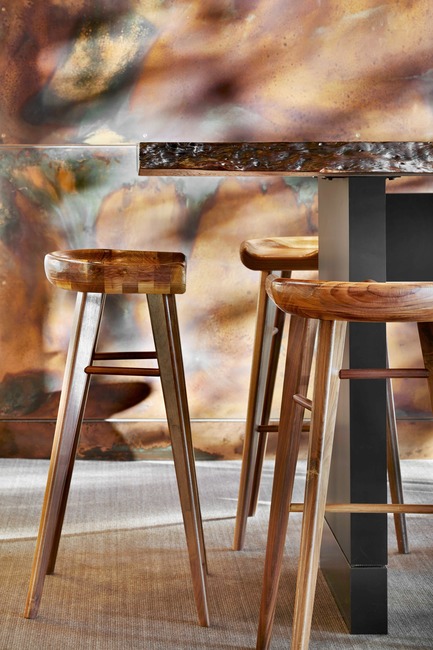 Press kit | 2886-02 - Press release | Wild Ginger Denny Triangle - SkB Architects - Commercial Interior Design - A custom made, live edge table from San Juan Ventures and wooden stools from&nbsp;Allmodern are set against a double-height wall adorned with patinated copper paneling - Photo credit: Drit Shoemaker