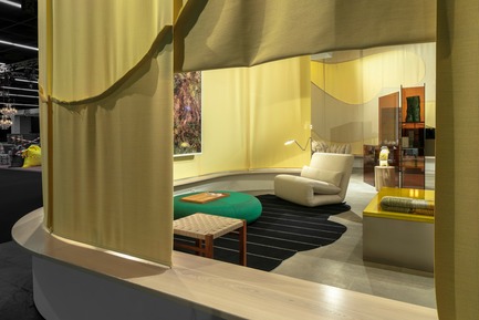 Press kit | 2704-05 - Press release | “Das Haus” 2019 at the imm cologne: Living by moods creates an appetite for open-plan homes - imm cologne 2019, Koelnmesse GmbH - Residential Interior Design - A view through a curtain “window” into the Reclining zone of “Living by Moods”, the Das Haus installation by Studio Truly Truly at imm cologne 2019. The low furniture, dark colours and soft shapes (Tattomi armchair, De Padova; Aswan stool, e15; Strata rug and Hatch pouf, prototypes by Studio Truly Truly) invite you to lay back and relax. - Photo credit: Constantin Meyer; Koelnmesse